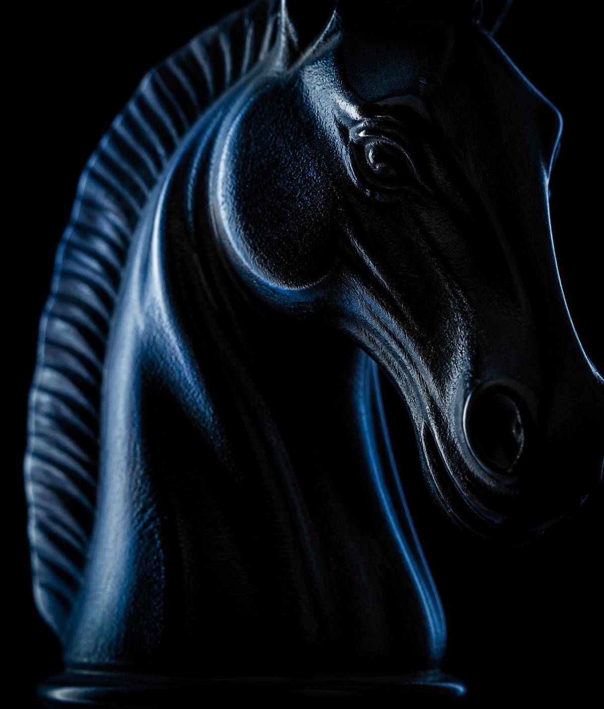 Close-up detail of an obsidian knight chess piece, rim-lit in blue against black